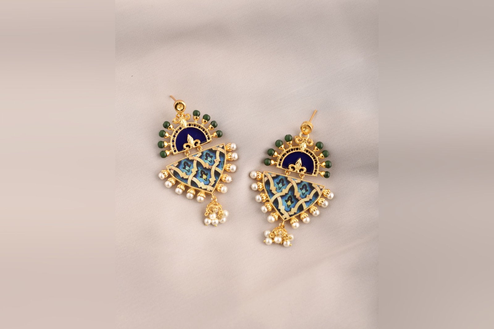 A pair of Blue-Green Arabesque earrings with navy enamelled crescents, painted blue tile panels, pearl borders and pearl jhumka drops, on blush silk.