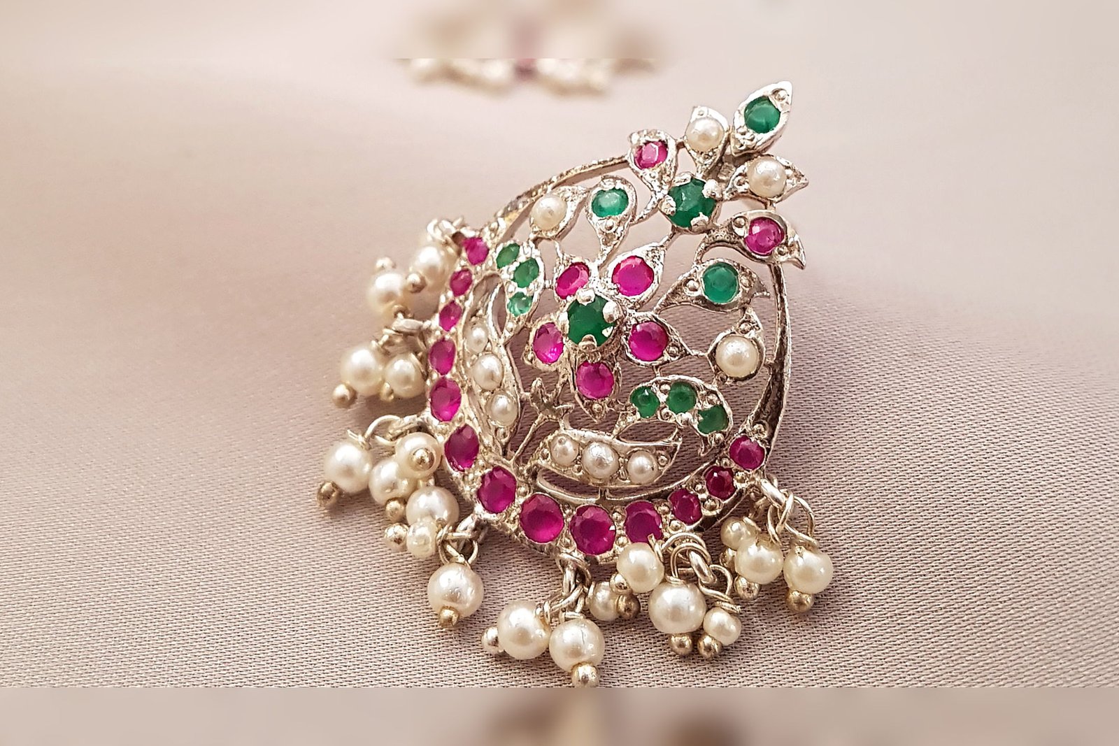A Ratan filigree earring in silver set with rubies, emeralds and pearls, on pink silk.