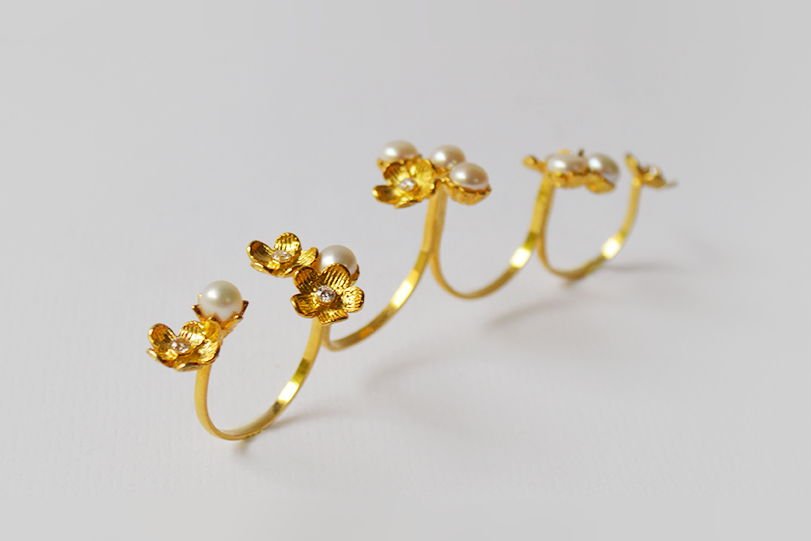 A Lei double ring in gold-plated silver with cast blossoms and pearls, on a white ground.