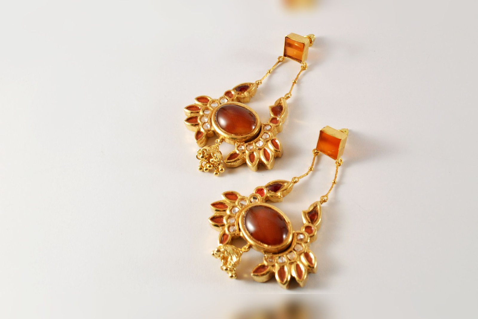A pair of Safari crab earrings with orange aqiq cabochons and enamelled detail, on a white ground.