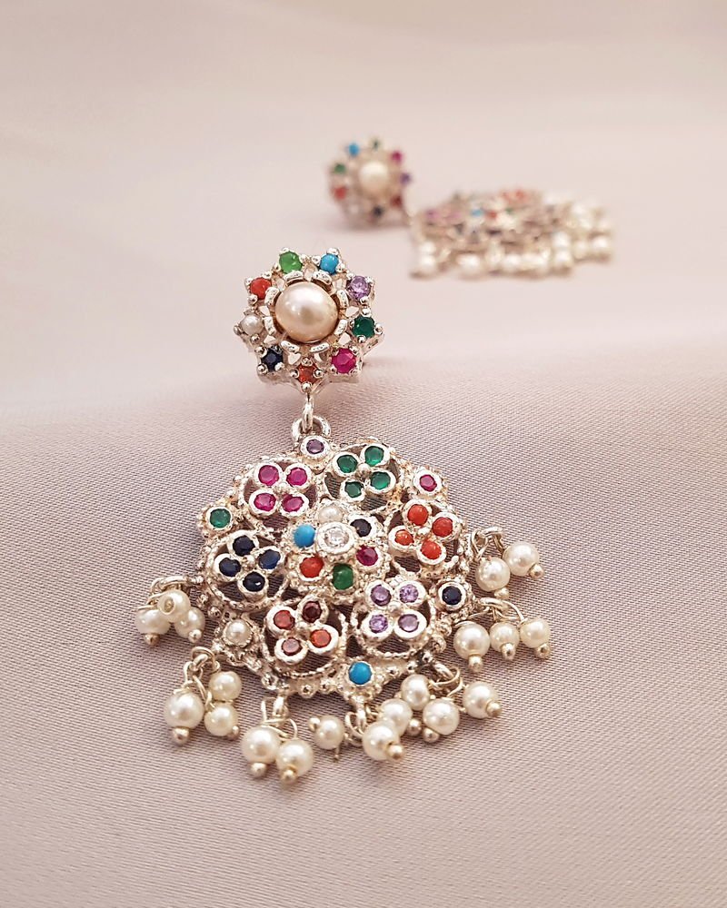 A Nauratan filigree earring in silver, its fan-shaped face set with nine colours of stones above a fringe of pearls.