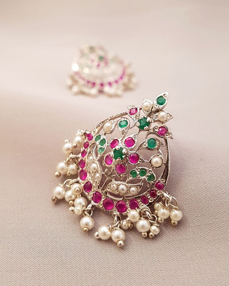 A Ratan filigree earring in silver with a scrolled paisley face set with rubies and emeralds and hung with pearls.