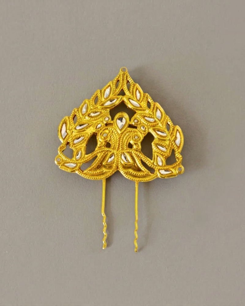 A Mumtaz peacock hair pin: a leaf-shaped gold-plated head set with kundan stones above two long prongs.