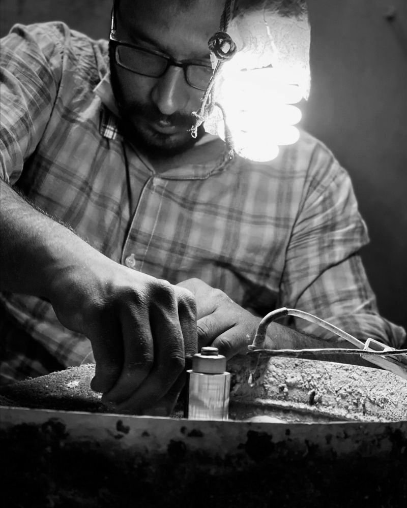 An artisan bent over the bench beneath a bare bulb, cutting and polishing a stone over the pitch bowl.